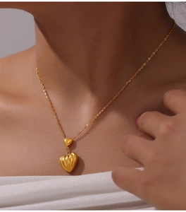 Detail view of layered heart pendants in gold plating worn on a cross chain necklace