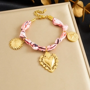 Détail du bracelet doré avec foulard en soie rose et pendentifs soleil et cœur