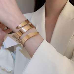 Close-up of golden geometric layered wide cuff bracelet on a white suit sleeve