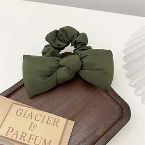 Close-up of a green satin bow scrunchie placed on a dark wooden tray with vintage props