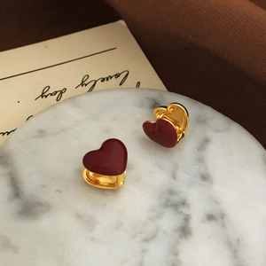 Detailed macro view of dark red enamel heart earrings with gold plated hoops on marble