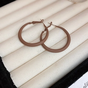 Macro view of oversized matte brown circular hoop earrings on a white velvet display tray