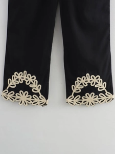 Gros plan sur les broderies florales beiges et les ourlets en crochet du pantalon noir ample
