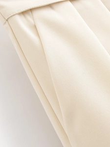 Close-up of high-waist beige trousers showing button detail and twill fabric texture