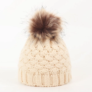 Detail shot of a cream-colored knitted infant hat with a plush dark brown pompom detail