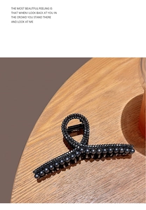 Detail of a black claw clip with dark pearl embellishments on a wooden stand
