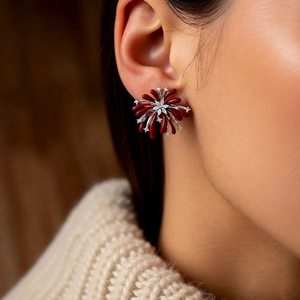 Detail of red fireworks stud earrings with zircon stones worn by a model in a cozy sweater