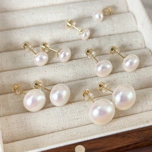 Minimalist white pearl stud earrings set with gold pins in various sizes on beige display
