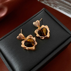Détail macro de boucles d'oreilles cœur avec œil de tigre et texture lave dorée sur coffret