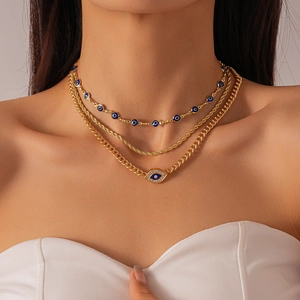 Detail of a three-layer gold necklace featuring rhinestone evil eye charms and cuban chains