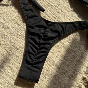 Detail view of black ribbed high-cut bikini bottom with ruched front design for women