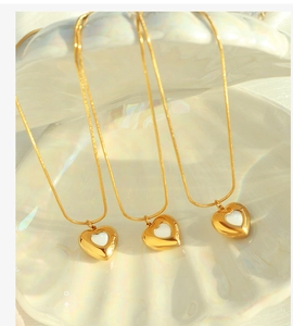 Detailed view of three gold heart necklaces with white shell inlay on a pearlescent tray