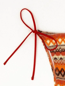 Detail showing the zigzag geometric knit pattern and vibrant red side ties on bikini bottoms