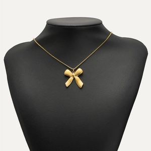 Golden stainless steel bow pendant necklace with ribbed texture shown on a black neck bust