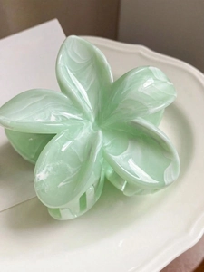Détail de la pince à cheveux fleurie vert clair avec texture marbrée sur plat blanc