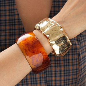 Close-up of amber resin marble bangle paired with gold wavy textured metal bracelet
