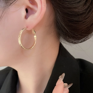 Close-up of elegant gold hoop earrings with fine diagonal twill texture on model