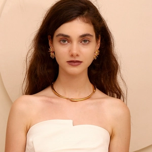 Close-up of gold starburst earrings with pink gemstones and a minimalist choker necklace