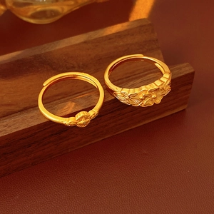 Dettaglio di due anelli vintage in oro opaco con motivi floreali e a croce su base di legno