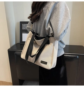 Beige canvas tote bag with wide black shoulder strap shown on a model for daily use