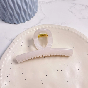 Close-up of a large pale pink shark hair clip with a gold metal spring on a ceramic plate