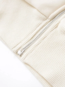 Close-up of metal zipper and ribbed cuffs on a cream-colored hooded sweatshirt