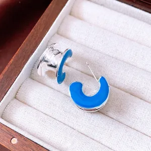 Silver C-shaped hoop earrings with vibrant blue enamel finish in a wooden jewelry box
