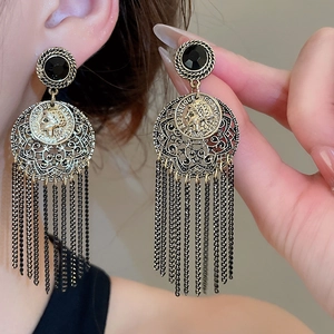 Close-up of vintage gold portrait coin earrings with black tassel chains and hollow patterns