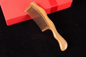 Close-up of green sandalwood comb with ergonomic handle on black background and red gift box