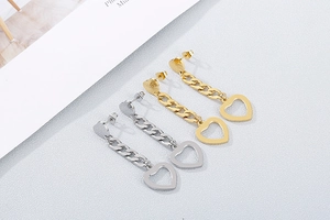 Detail of heart stud earrings with chains in gold and silver finish on grey background