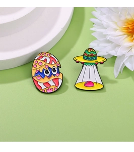 Close-up of enamel dinosaur egg and UFO pins on a light green background with floral decor