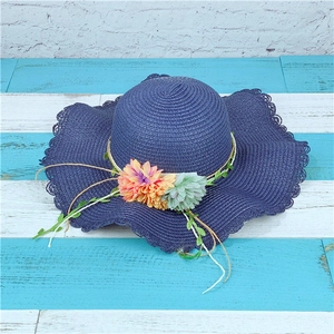 Detail of navy straw sun hat featuring wavy brim and delicate decorative flowers