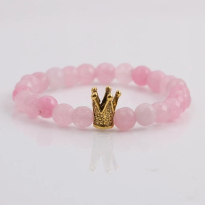 Facettiertes rosa Steinperlenarmband mit goldener Krone auf weißem Hintergrund