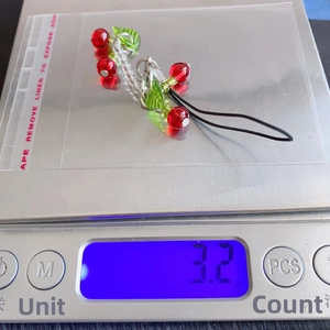 Detailed view of handmade glass cherry charm on scale weighing approximately 3.2g