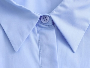 Detail of light blue poplin shirt collar featuring crisp fabric texture and matching button