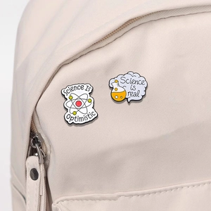 Science Is Optimistic enamel pins with atom and flask motifs on a beige backpack