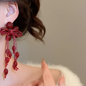 Close-up of red resin bow earrings with long tassels and glossy berry-like beads