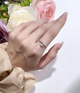 Close-up of emerald cut moissanite ring worn on finger with floral background