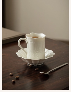Close-up of white ceramic coffee cup and saucer with floral embossed petal edges