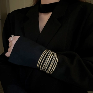 Detail of layered gold geometric bangles and irregular silver ring on black suit sleeve