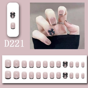Detail of nude pink press-on nails with black French tips and 3D bow accent