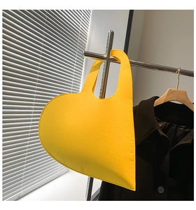 Detail of a bright yellow heart-shaped felt handbag with a stylish integrated handle