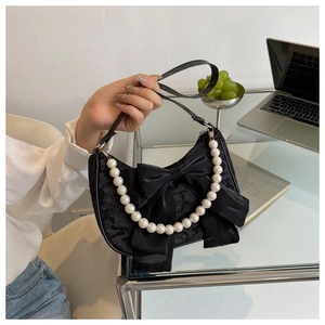 Detail of elegant black ribbon bow and pearl chain on a textured fabric handbag