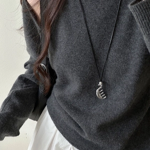 Minimalist silver comb pendant necklace on black cord paired with a grey knit sweater