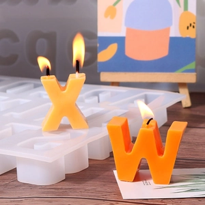 Macro view of alphabet silicone molds and burning orange letter candles on a wooden table