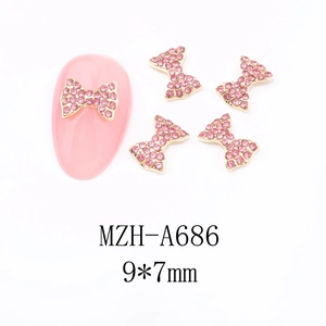 Macro shot of 9x7mm gold bow nail charm with pink rhinestones for festive manicure