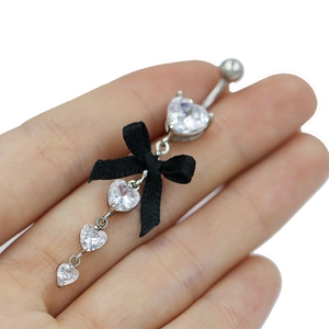 Gros plan d'un piercing de nombril en cœur avec nœud noir tenu dans la main pour taille