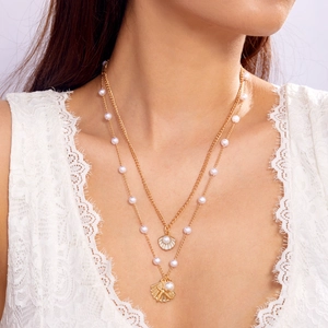 Close-up of a double-layered gold necklace with pearls and sea shell charms on a model