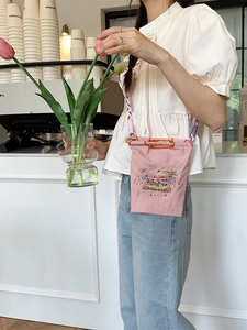 Pink embroidered crossbody bag with carousel pattern and woven strap in a cafe setting