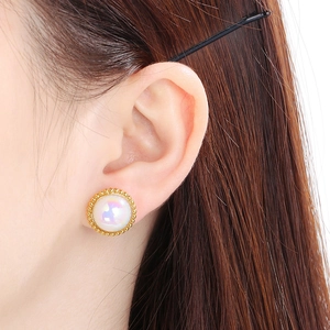 Close-up of a gold stud earring with iridescent shell inlay worn by a model